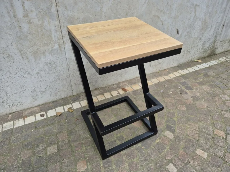 Sgabello da bar in ferro nero e seduta in rovere, con il telaio a Z e il poggiapiedi, su un pavimento di porfido (foto ritoccata con un'AI generativa)
