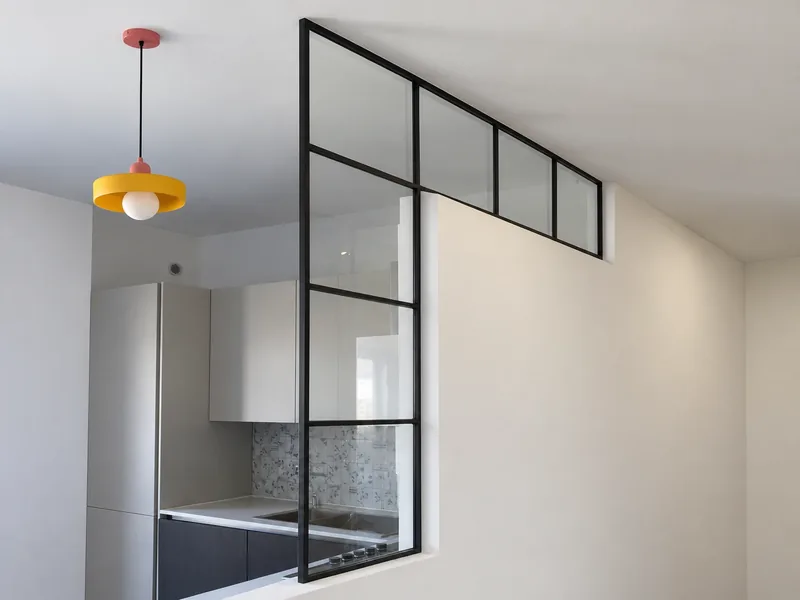 Vetrata a L in ferro nero e vetro tra soggiorno e cucina, sopra un muretto bianco fino al soffitto (foto ritoccata con un'AI generativa)